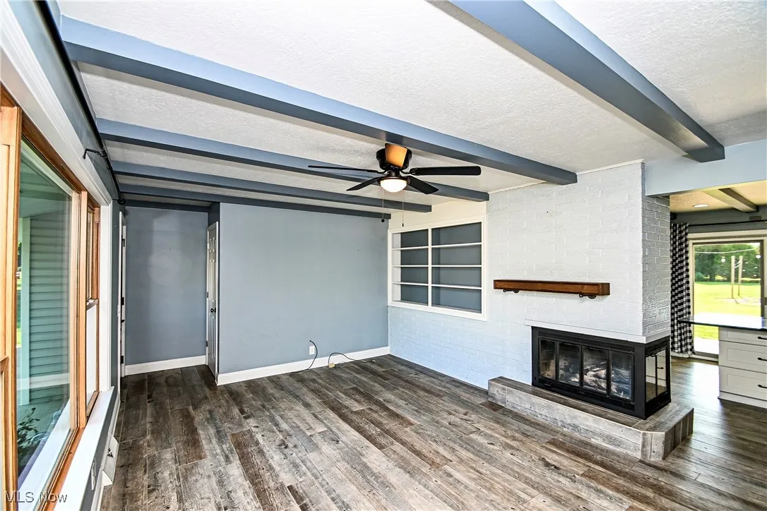 Unfurnished living room featuring a textured ceiling, a brick fireplace, dark wood-type flooring, ceiling fan, and beamed ceiling