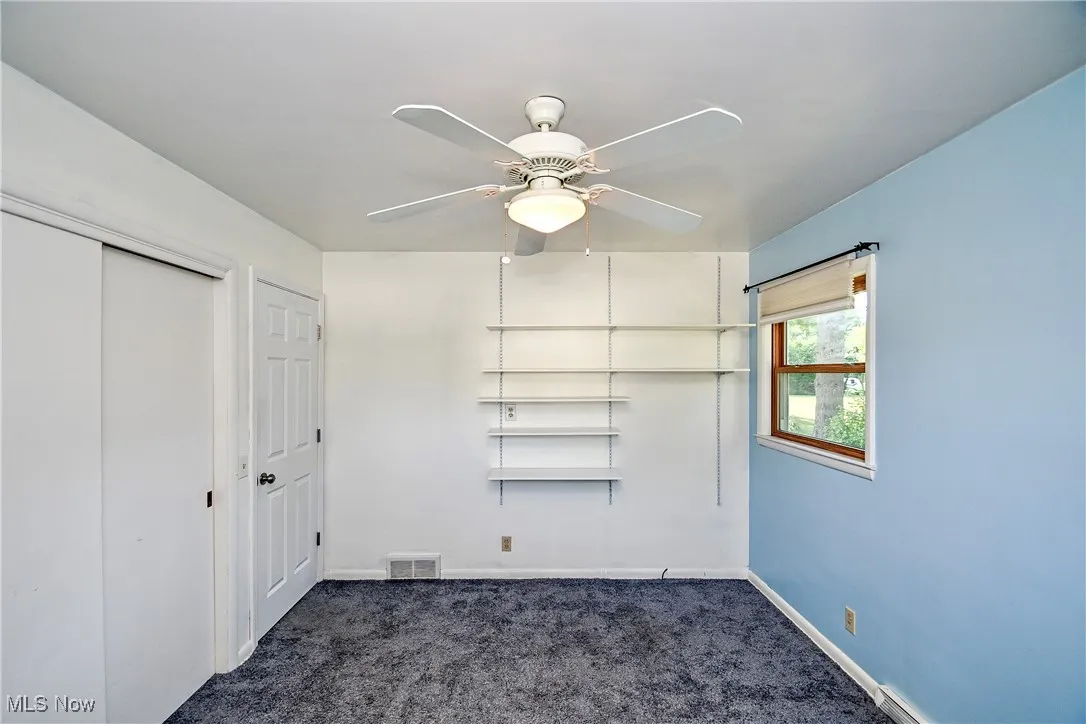 Unfurnished bedroom with dark carpet, a closet, and a ceiling fan