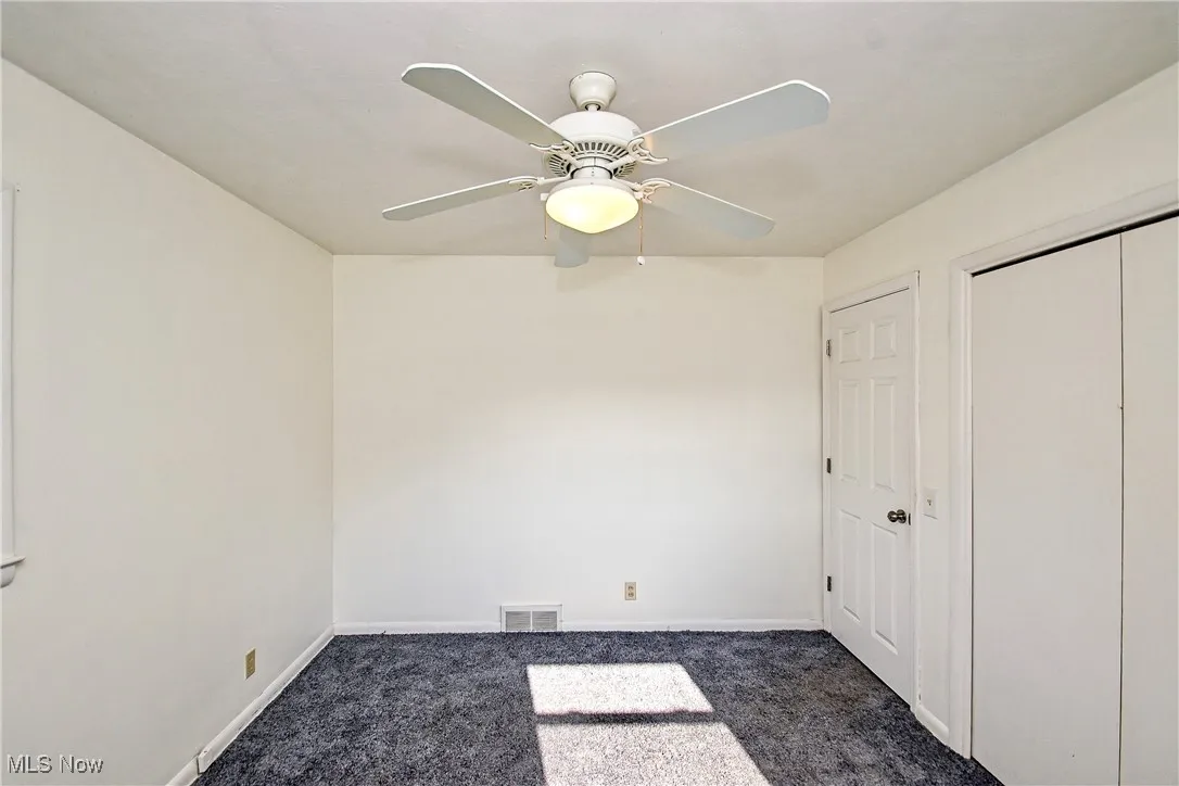 Unfurnished bedroom with dark carpet, a ceiling fan, and a closet