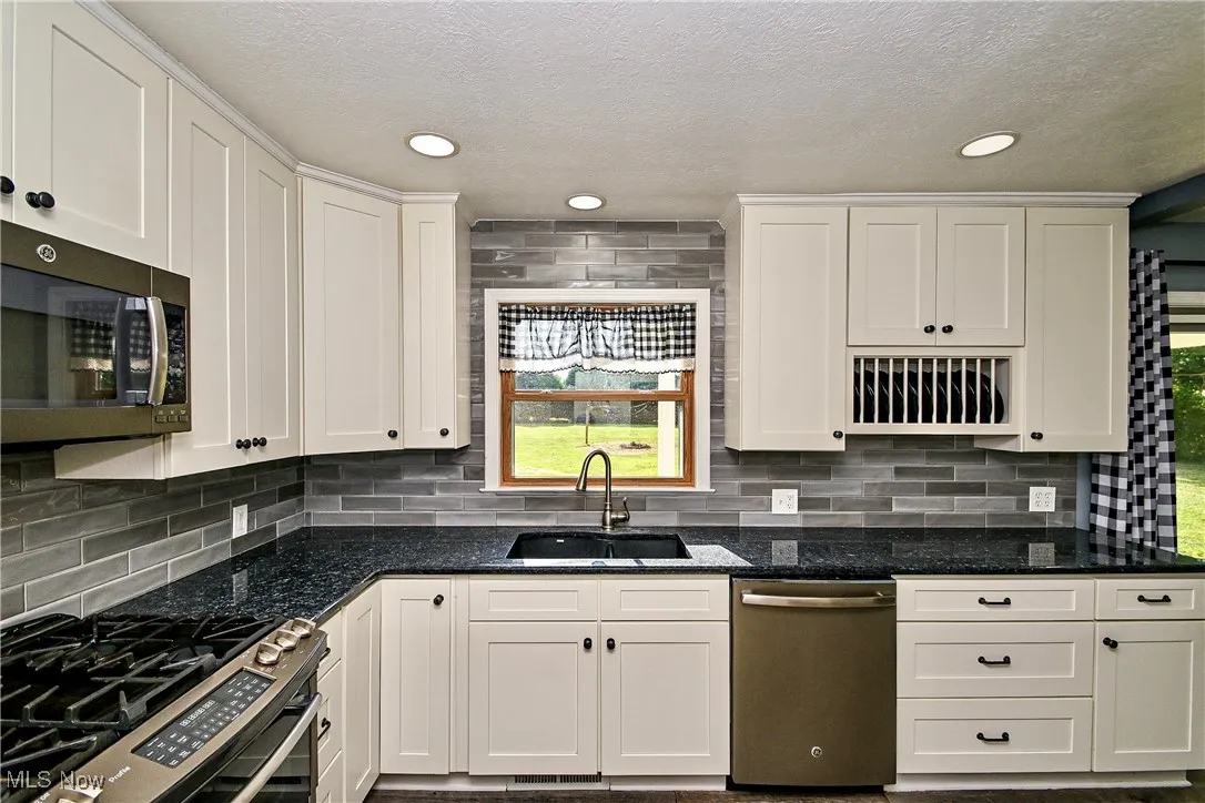 Kitchen with appliances with stainless steel finishes, dark stone countertops, white cabinets, a textured ceiling, and recessed lighting