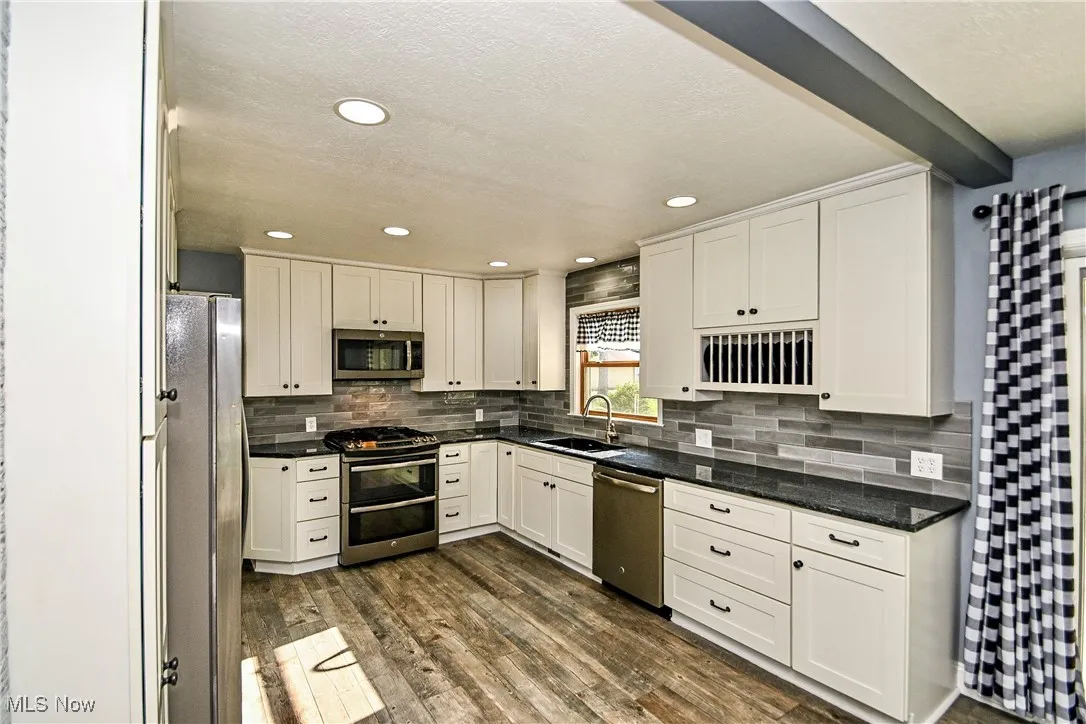 Kitchen featuring white cabinetry, appliances with stainless steel finishes, dark wood-type flooring, beam ceiling, and decorative backsplash