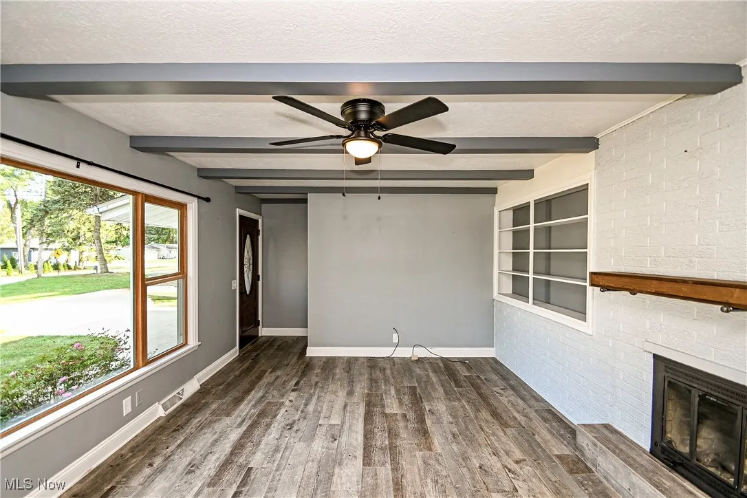 Unfurnished living room featuring beam ceiling, brick wall, wood finished floors, a textured ceiling, and a brick fireplace