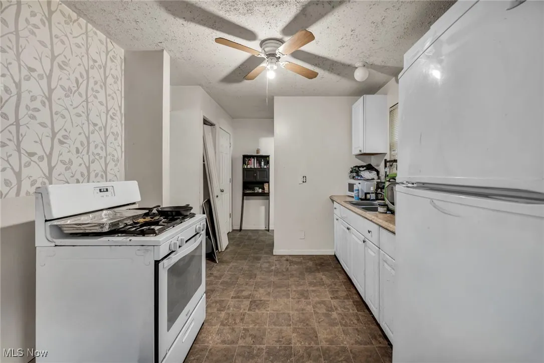 Kitchen featuring white appliances, light countertops, white cabinets, a ceiling fan, and a textured ceiling