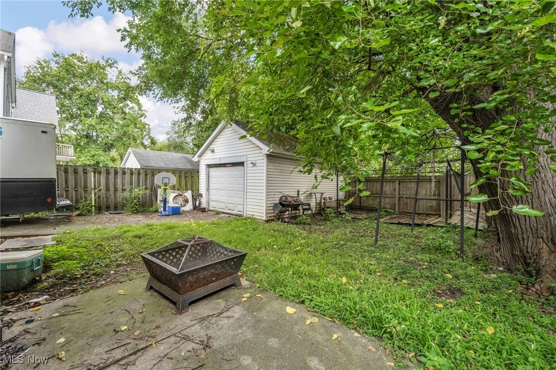 Fenced backyard featuring an outdoor fire pit, an outbuilding, a detached garage, and a patio area