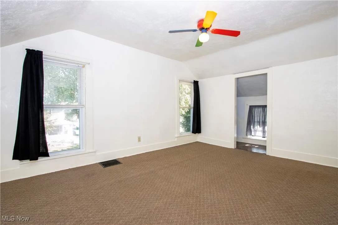 Empty room with vaulted ceiling, a textured ceiling, and carpet floors