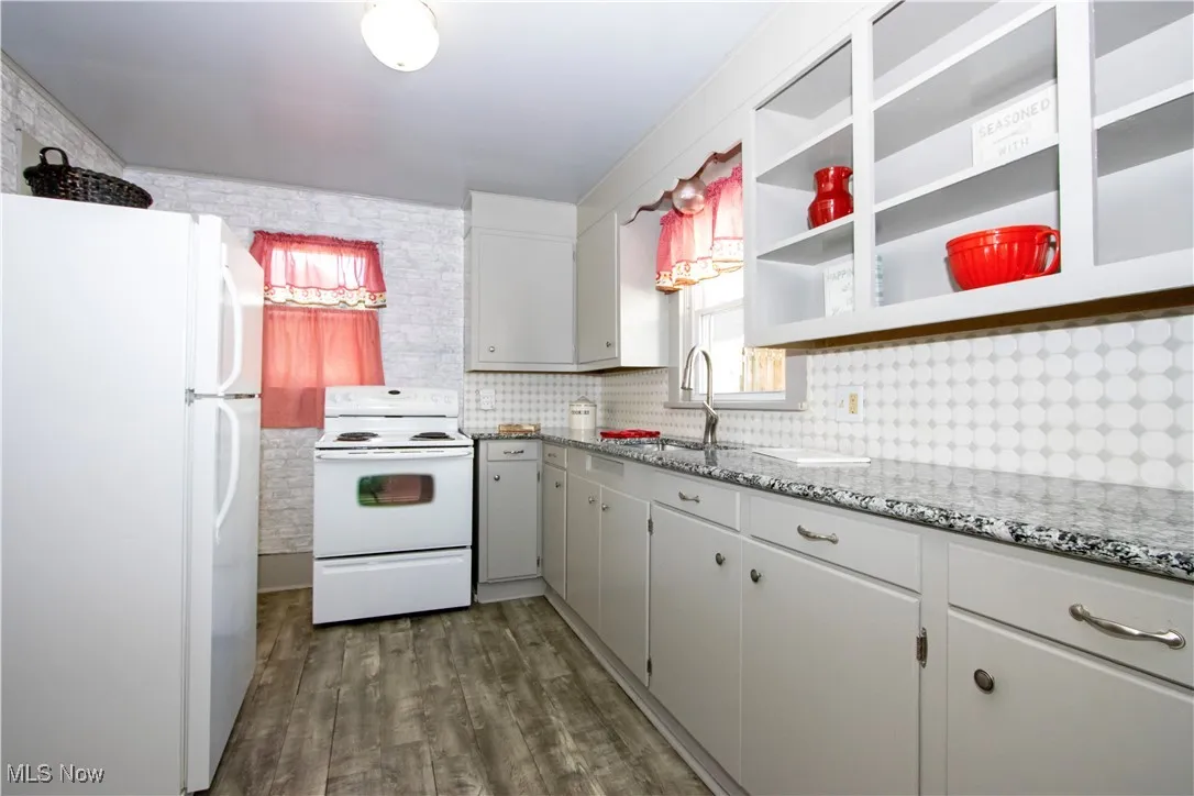 Kitchen featuring white appliances, light stone countertops, dark wood-style flooring, tasteful backsplash, and open shelves