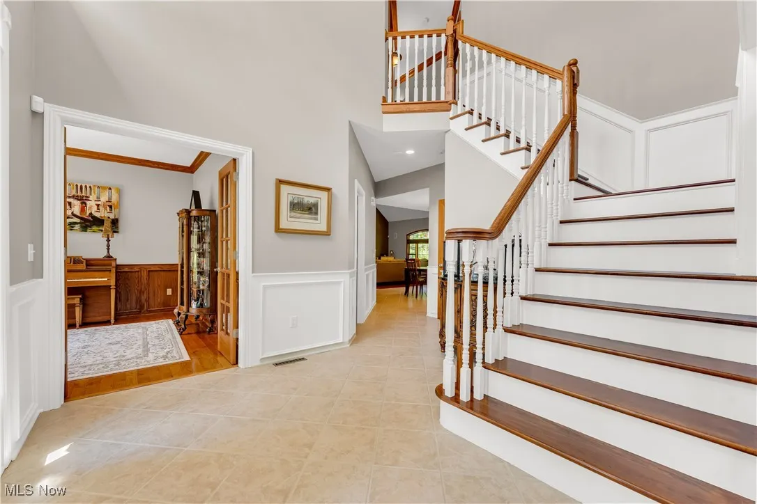 2 story foyer entrance featuring a wainscoted wall & ceramic tile floor