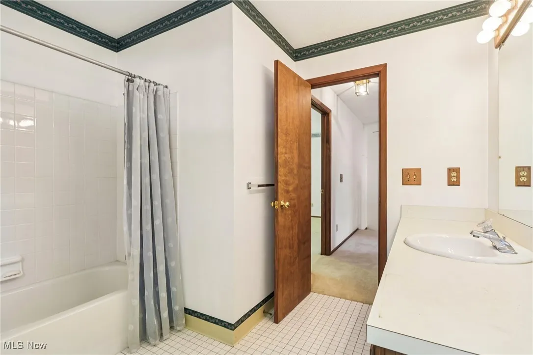 Full bathroom with shower / bathtub combination with curtain, vanity, light tile patterned floors, and ornamental molding