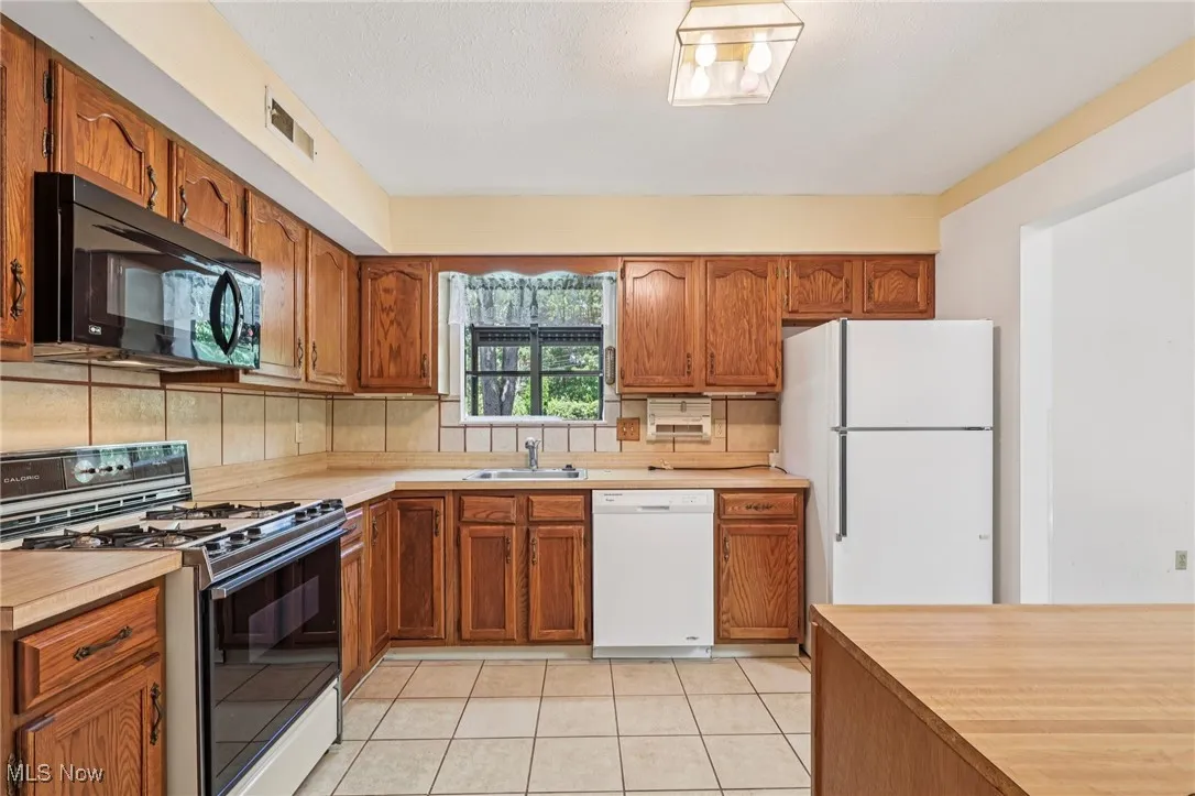 Kitchen with white appliances, brown cabinets, light tile patterned flooring, light countertops, and tasteful backsplash