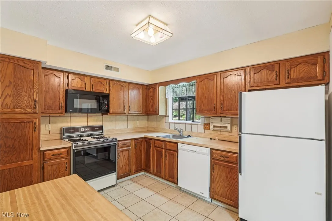 Kitchen with brown cabinetry, white appliances, light countertops, light tile patterned floors, and tasteful​​‌​​​​‌​​‌‌​‌‌​​​‌‌​‌​‌​‌​​​‌​​ backsplash
