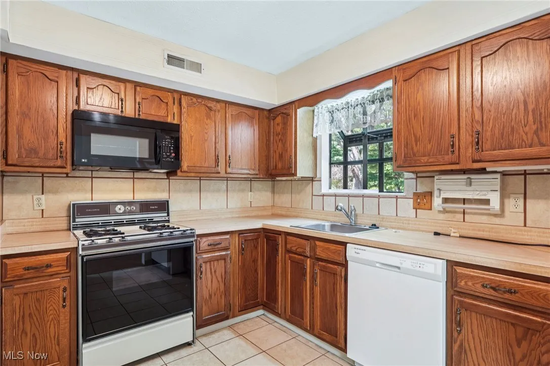 Kitchen featuring brown cabinets, light countertops, white dishwasher, and black microwave