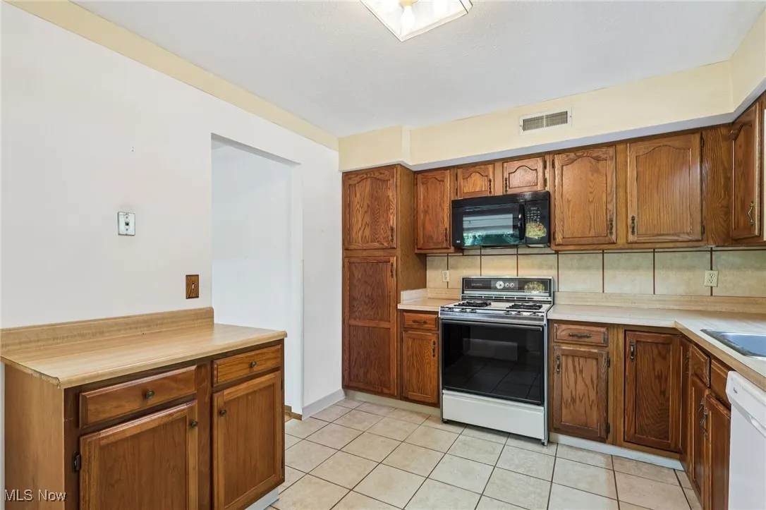 Kitchen featuring light countertops, white appliances, light tile patterned flooring, brown cabinets, and decorative backsplash