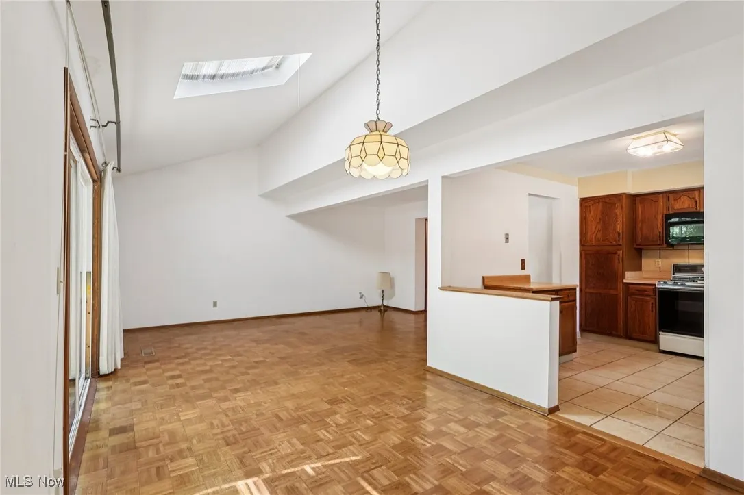 Kitchen with a skylight, brown cabinetry, decorative light fixtures, white stove, and black microwave