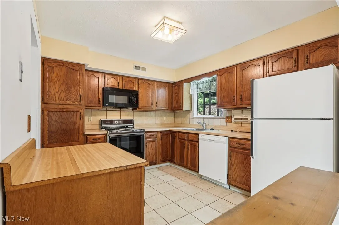 Kitchen featuring white appliances, brown cabinets, decorative backsplash, light tile patterned floors, and a peninsula