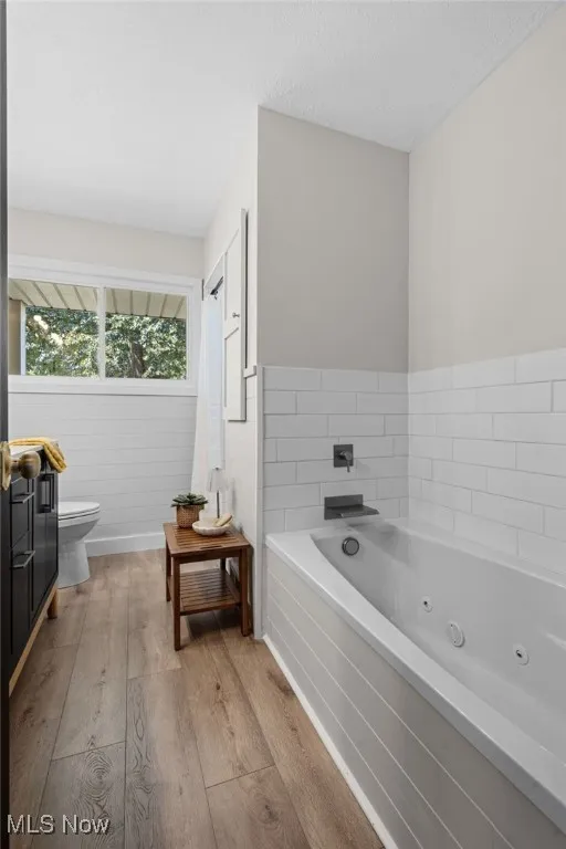 Full bathroom on main floor featuring a jetted tub, laminate floors, vanity, and a separate shower