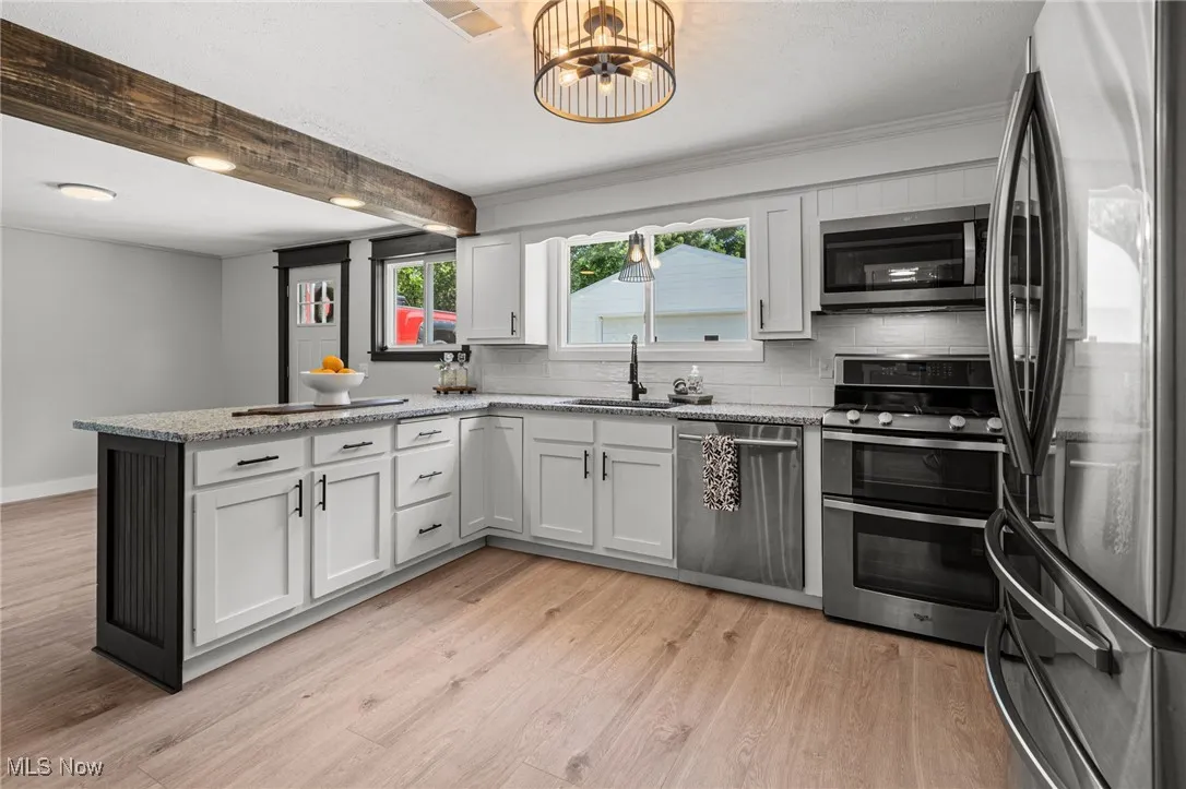 Kitchen with stainless steel appliances, a peninsula, beamed ceiling, decorative backsplash, and laminate finished floors