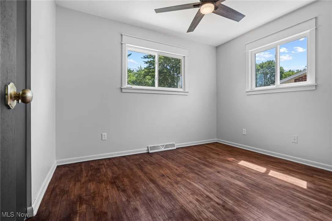 Primary bedroom with dark wood-style floors, plenty of natural light, and ceiling fan/light