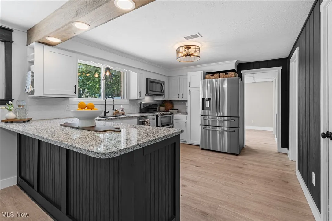 Kitchen featuring stainless steel appliances, a peninsula, granite countertops, ornamental molding, and light laminate floors