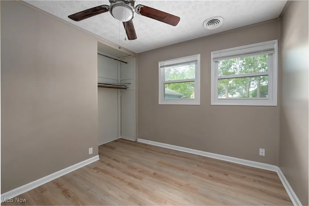 Unfurnished bedroom with light wood-style flooring, a textured ceiling, a closet, and ceiling fan
