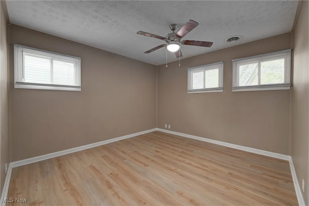 Unfurnished room featuring a textured ceiling, light wood-style floors, and a ceiling fan