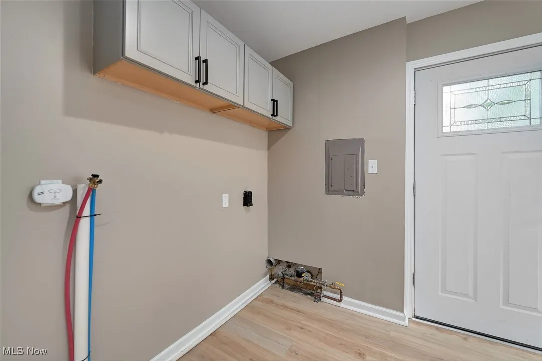 Washroom with cabinet space, washer hookup, light wood-style flooring, and electric panel