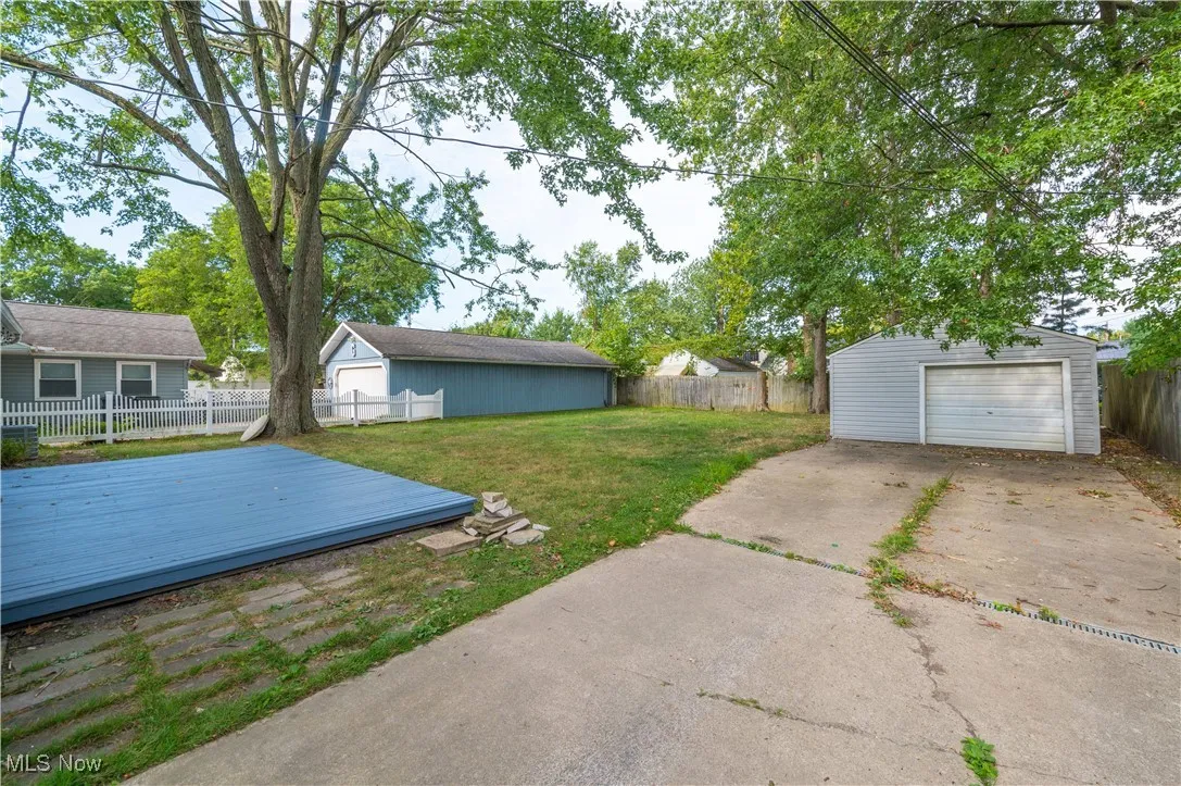 Fenced backyard featuring a garage, an outbuilding, a deck, and driveway