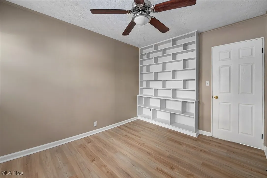 Empty room with a textured ceiling, light wood-style floors, a ceiling fan, and built in features