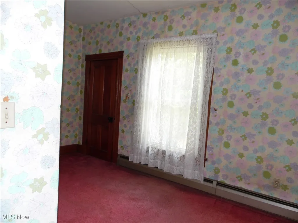 Spare room featuring a baseboard radiator, carpet flooring, and wallpapered walls