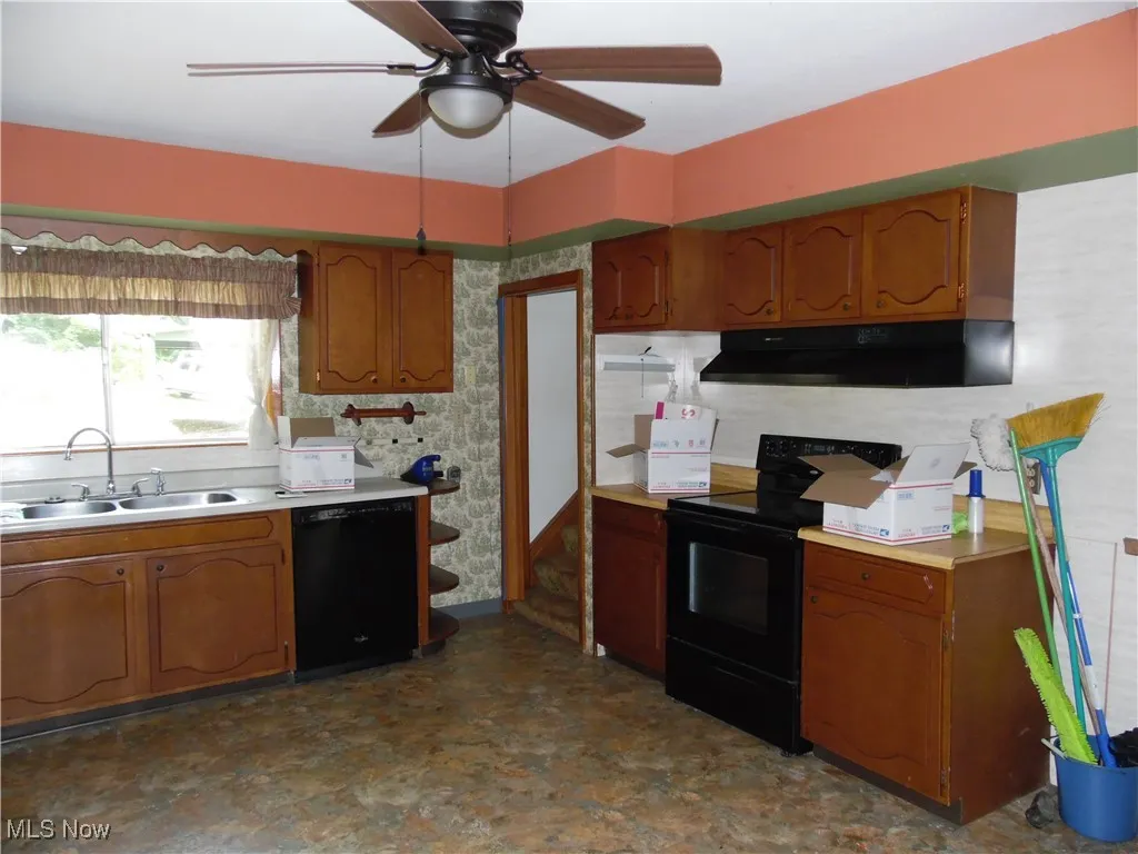 Kitchen with black appliances, brown cabinets, wallpapered walls, light countertops, and under cabinet range hood