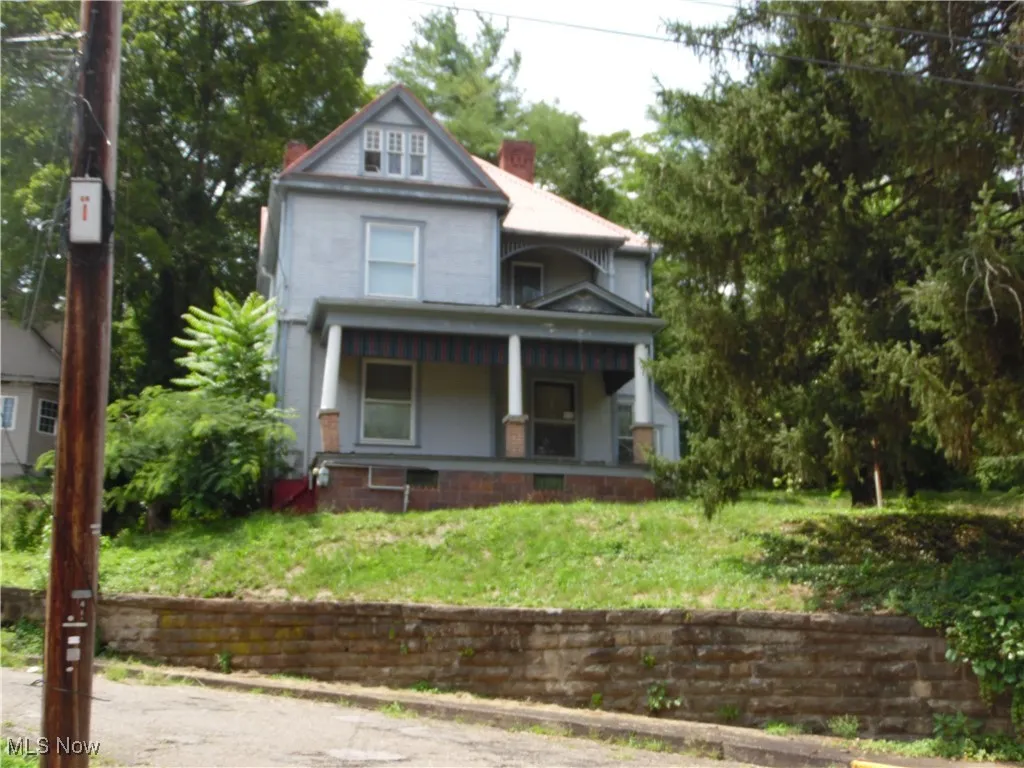 View of front of property featuring a chimney, covered porch, and a front yard