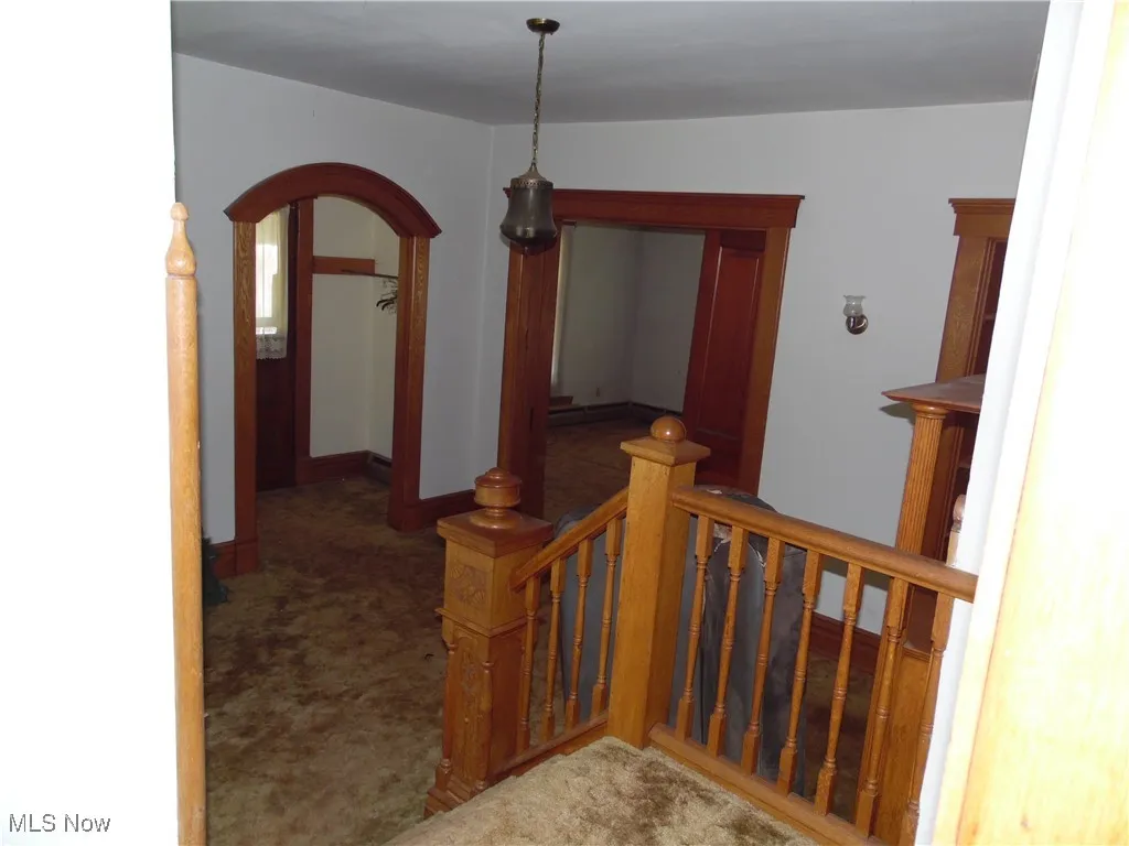 Hall with carpet, arched walkways, and an upstairs landing
