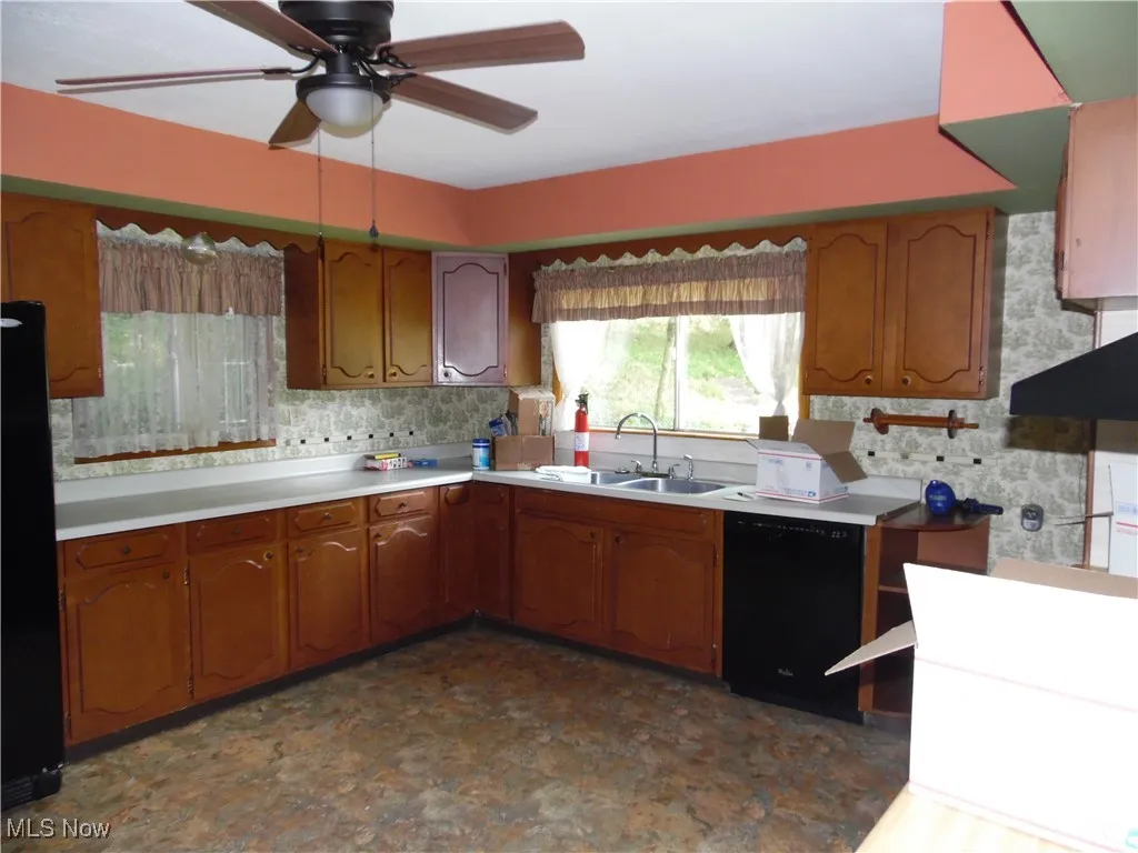 Kitchen with brown cabinets, light countertops, black appliances, a ceiling fan, and dark floors