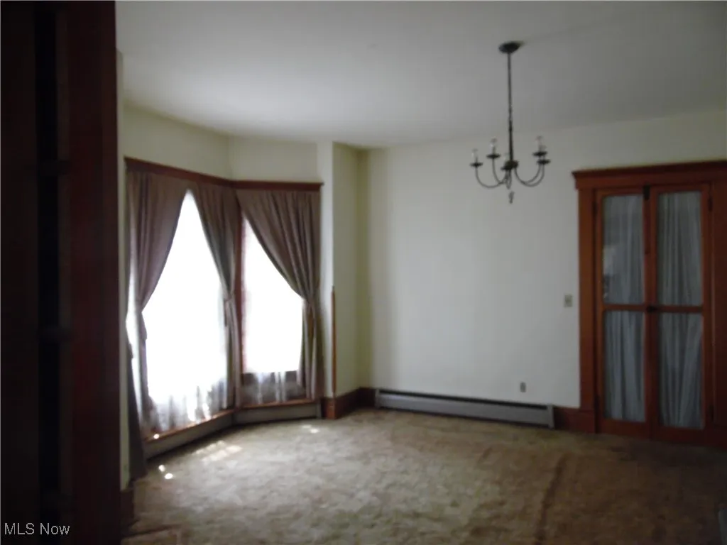 Unfurnished dining area with a chandelier, a baseboard heating unit, and carpet floors