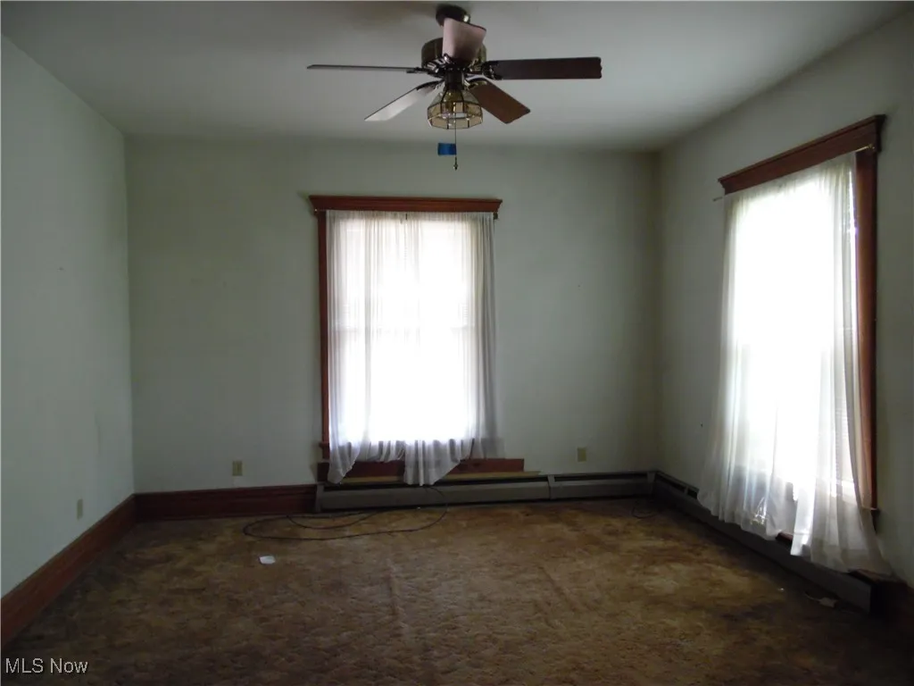 Unfurnished room featuring dark carpet, ceiling fan, and baseboard heating