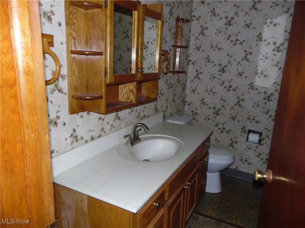 Half bathroom featuring wallpapered walls and vanity