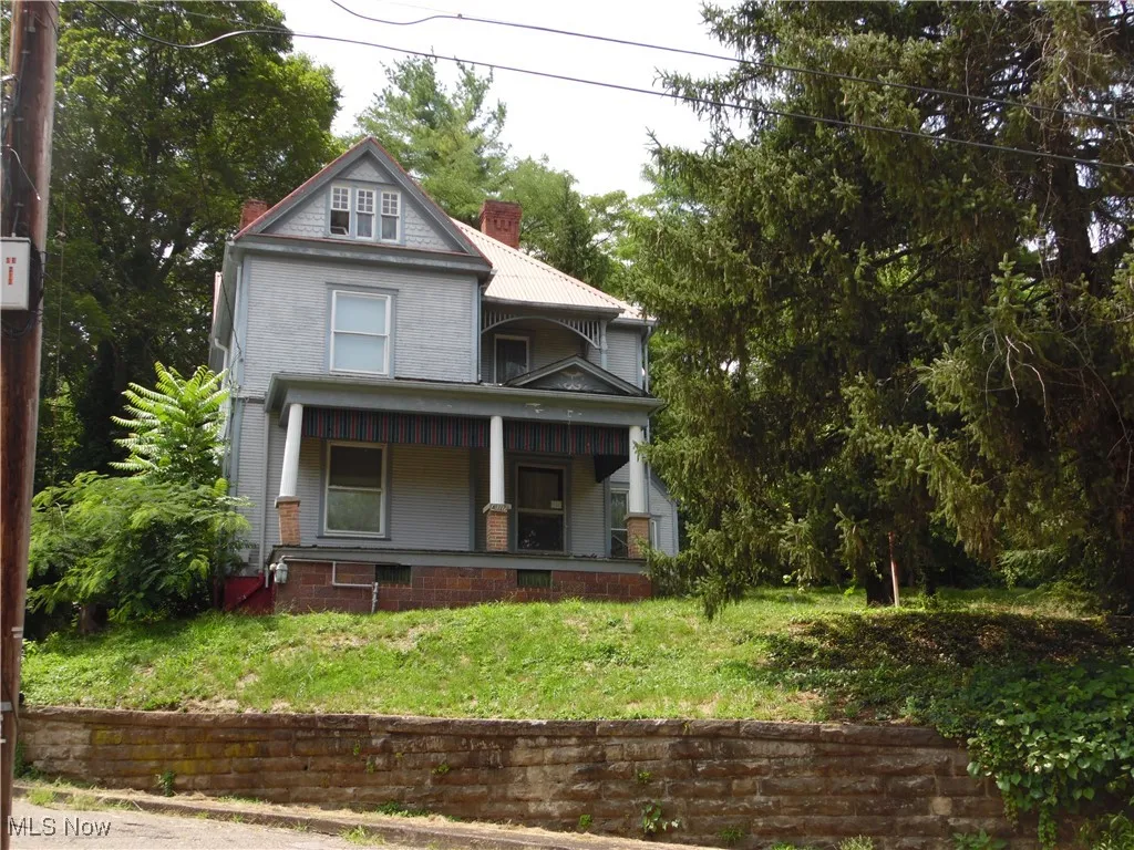 Victorian-style house featuring a chimney, a porch, and a front lawn