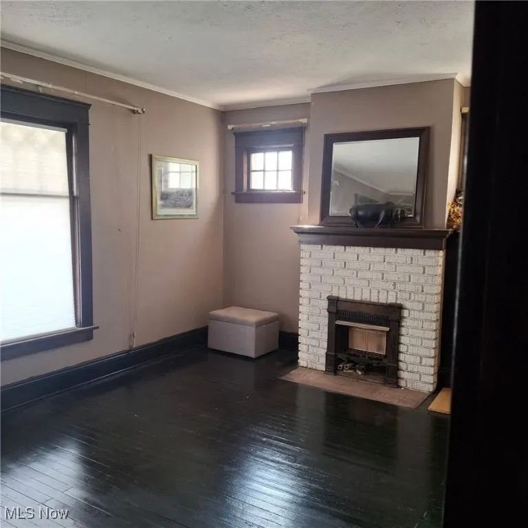 Unfurnished living room featuring dark wood-type flooring, ornamental molding, a brick fireplace, and a textured ceiling