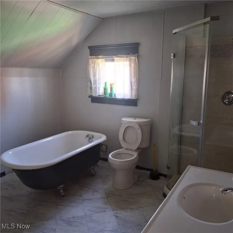 Bathroom with a stall shower, a soaking tub, light marble finish flooring, and vaulted ceiling