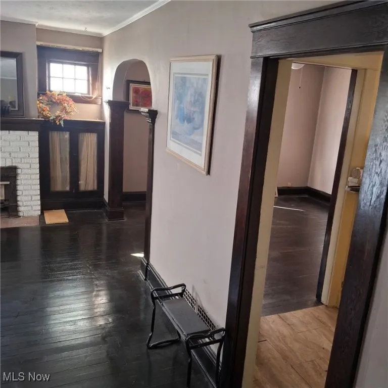 Hallway featuring hardwood / wood-style floors, crown molding, and arched walkways