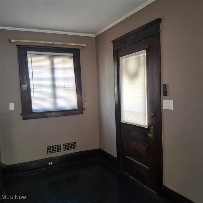 Foyer entrance featuring healthy amount of natural light, ornamental molding, and dark wood-style flooring