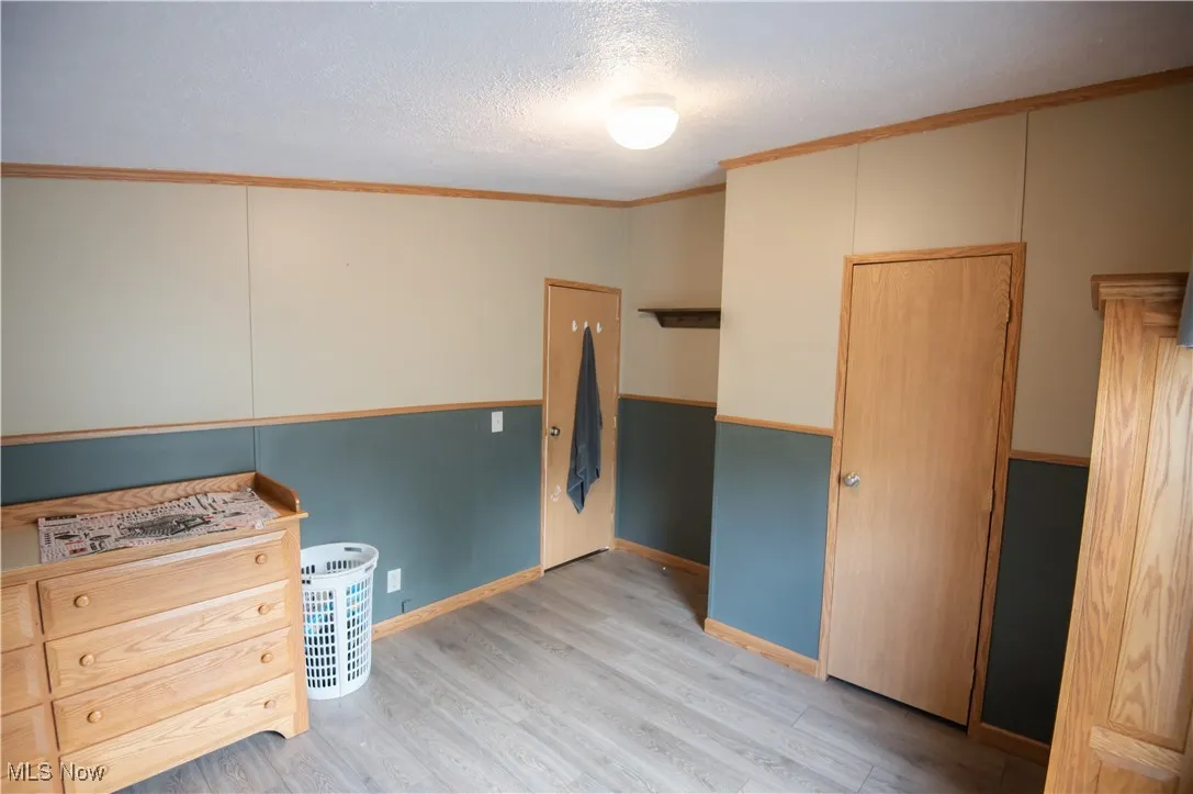 Unfurnished bedroom with crown molding, light wood-style floors, and a textured ceiling