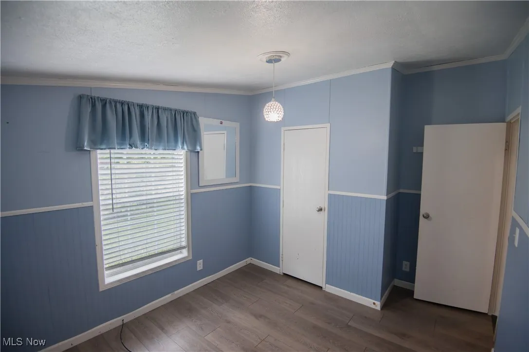 Unfurnished bedroom featuring crown molding, dark wood-style flooring, a textured ceiling, and wainscoting