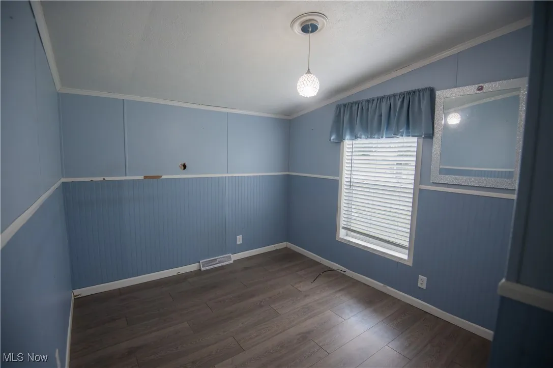 Unfurnished room featuring dark wood-type flooring, ornamental molding, and vaulted ceiling