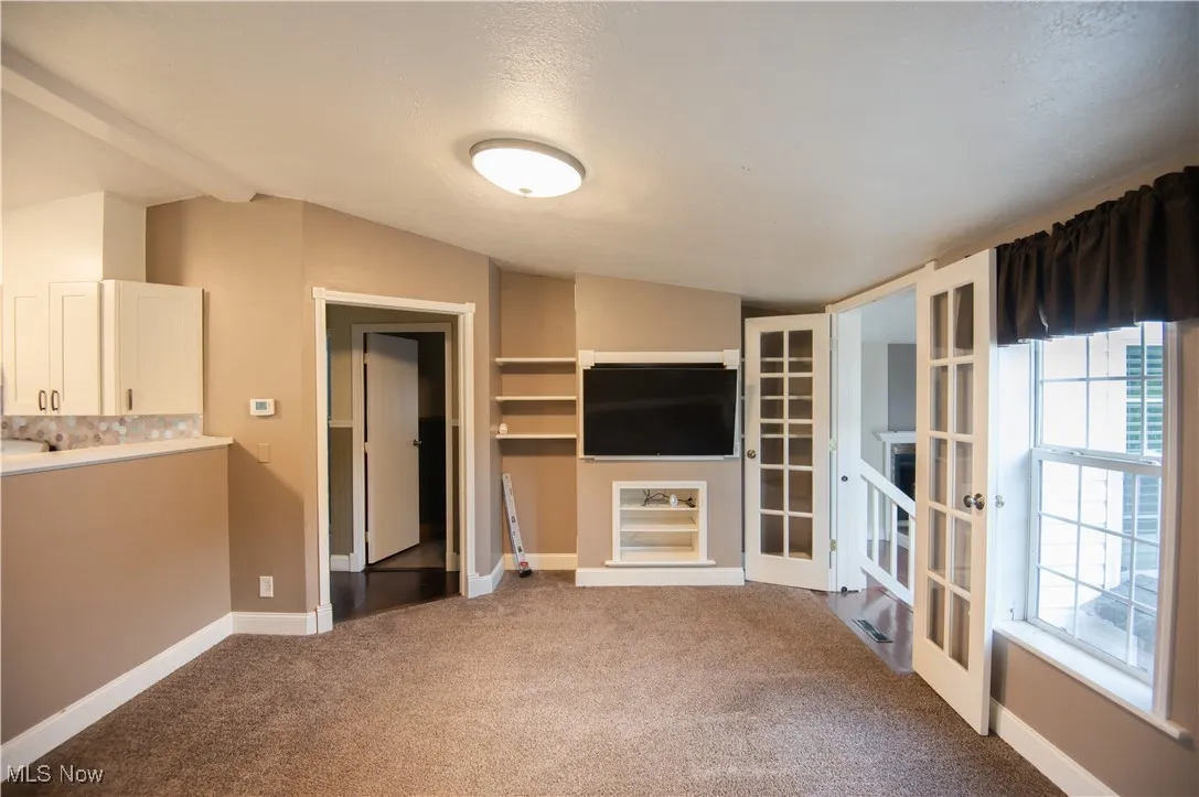 Unfurnished living room with light carpet, french doors, and a textured ceiling