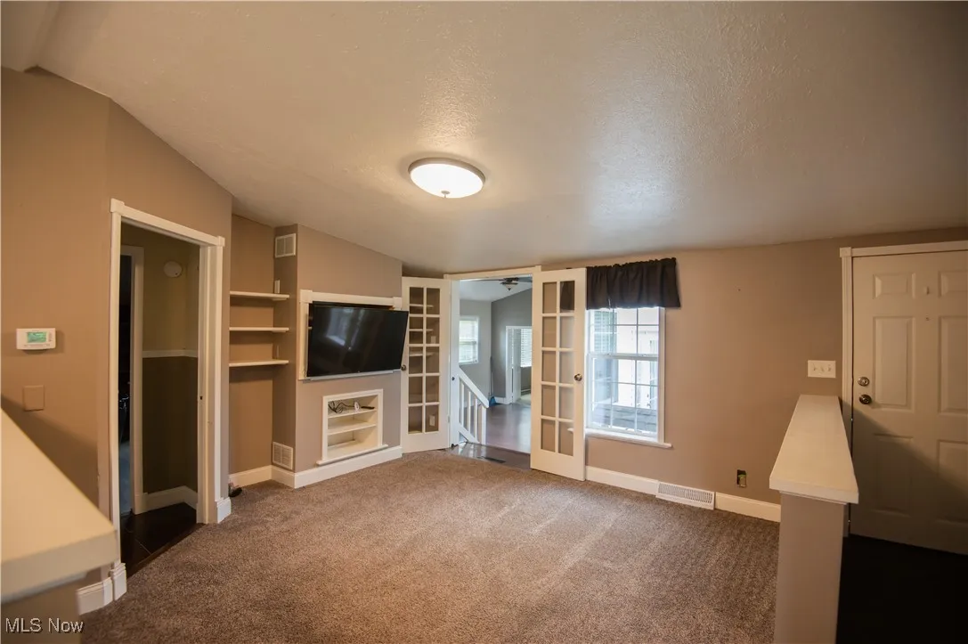 Unfurnished living room featuring a textured ceiling, vaulted ceiling, dark carpet, and built in shelves