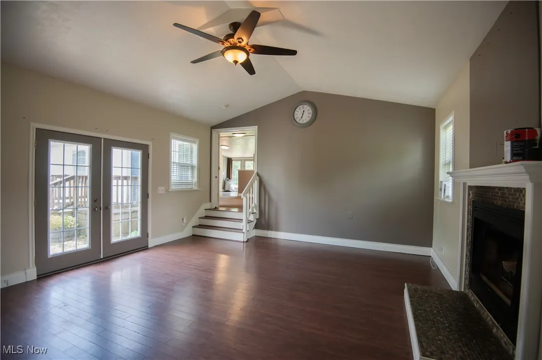 Unfurnished living room with stairs, vaulted ceiling, dark wood-type flooring, ceiling fan, and a brick fireplace