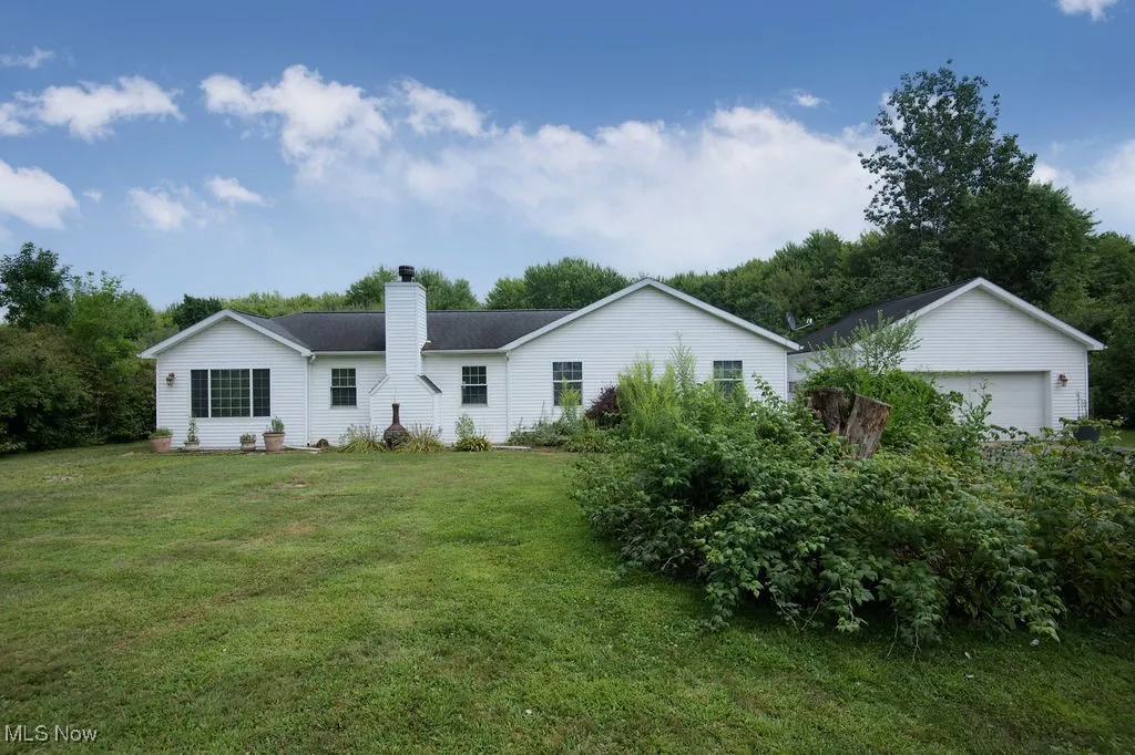 Front view of property with a chimney, a yard, a garage, and an outbuilding
