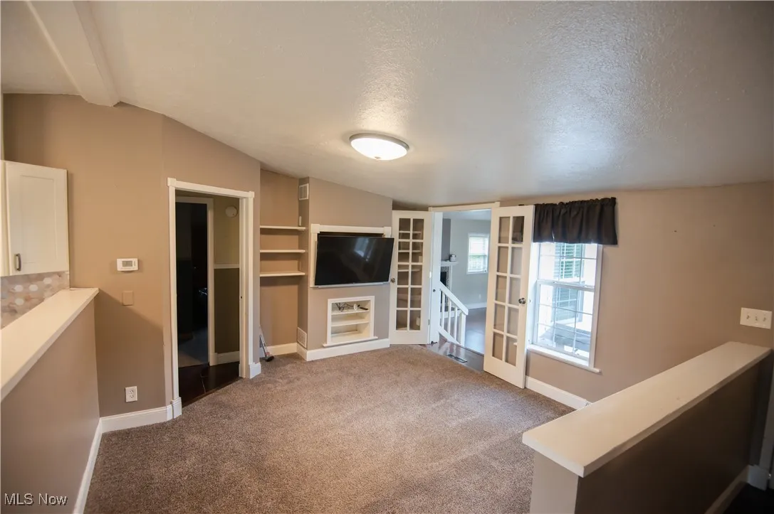 Unfurnished living room with lofted ceiling, dark colored carpet, and a textured ceiling