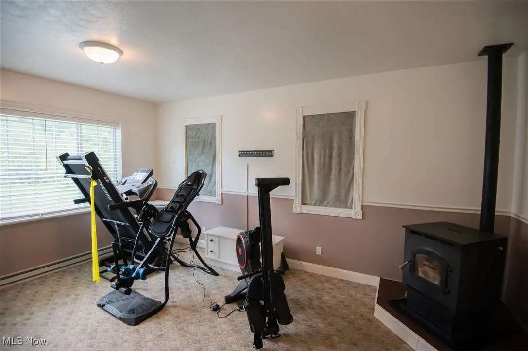 Exercise room with a wood stove, carpet, and a baseboard heating unit. 4th bedroom