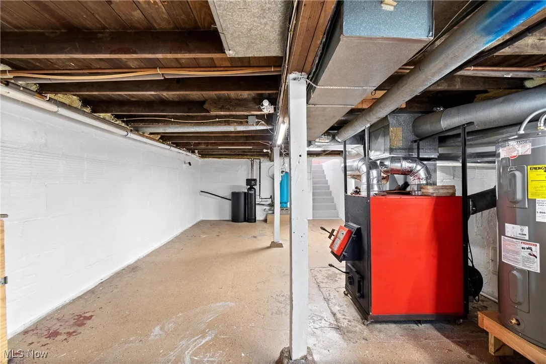 Unfinished below grade area featuring electric water heater, heating unit, stairs, and a water softener system
